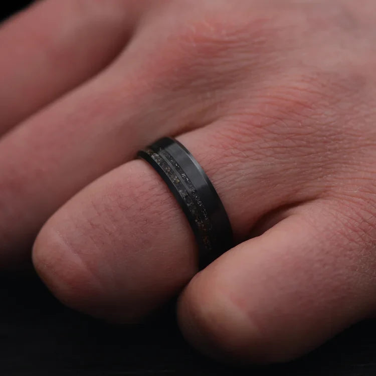 Hand wearing a 7mm Zirconium Wedding Band featuring unique crushed T-Rex bone and meteorite inlays, brushed bevel profile, mens ring with free engraving option.