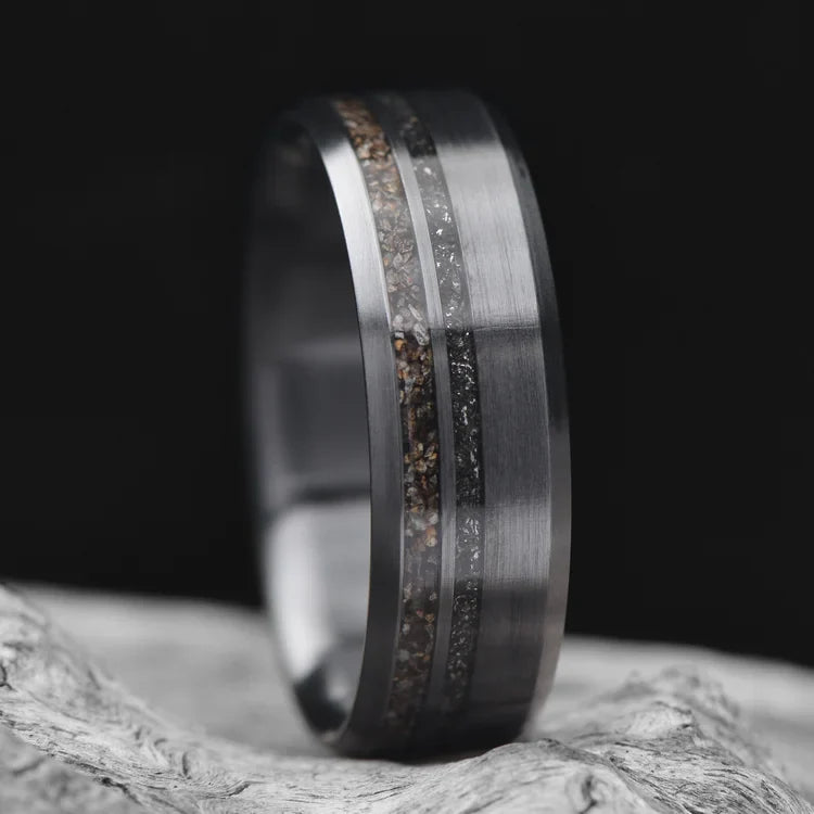 Zirconium wedding band with crushed T-Rex and meteorite inlays, 7mm mens ring with unique brushed bevel profile, displayed on a white sea branch, free engraving available.