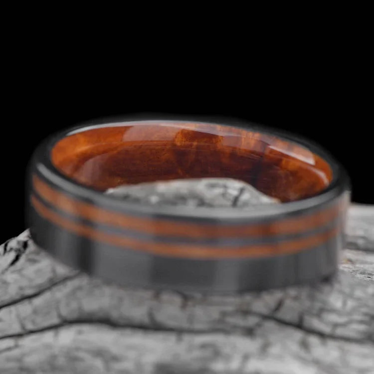 Black titanium wedding band with Western maple burl inlays, featuring a unique brushed finish, displayed on a white sea branch; 7mm mens ring with free engraving option.