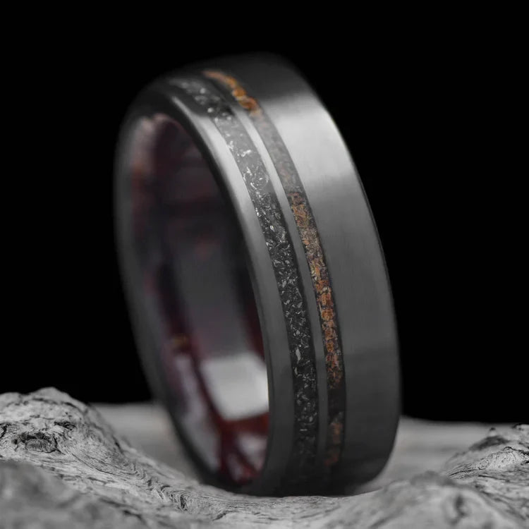 Black titanium wedding band with meteorite and crushed T-Rex inlays, 7mm mens matte flat profile ring, unique design, laying on white sea branch, free engraving available.