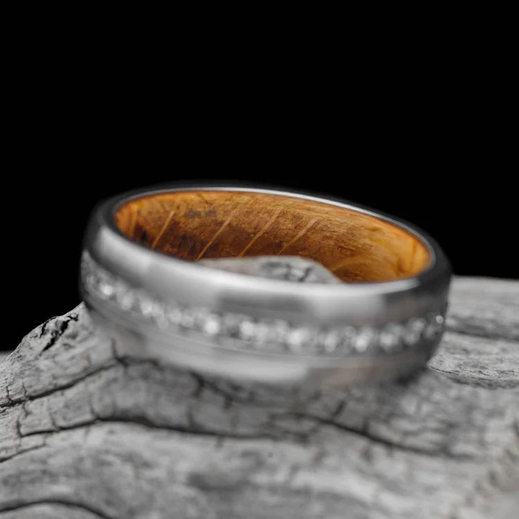 Brushed titanium wedding band with whiskey barrel oak inner sleeve and eternity set stones, 7mm mens ring, displayed on a white sea branch, free engraving available.