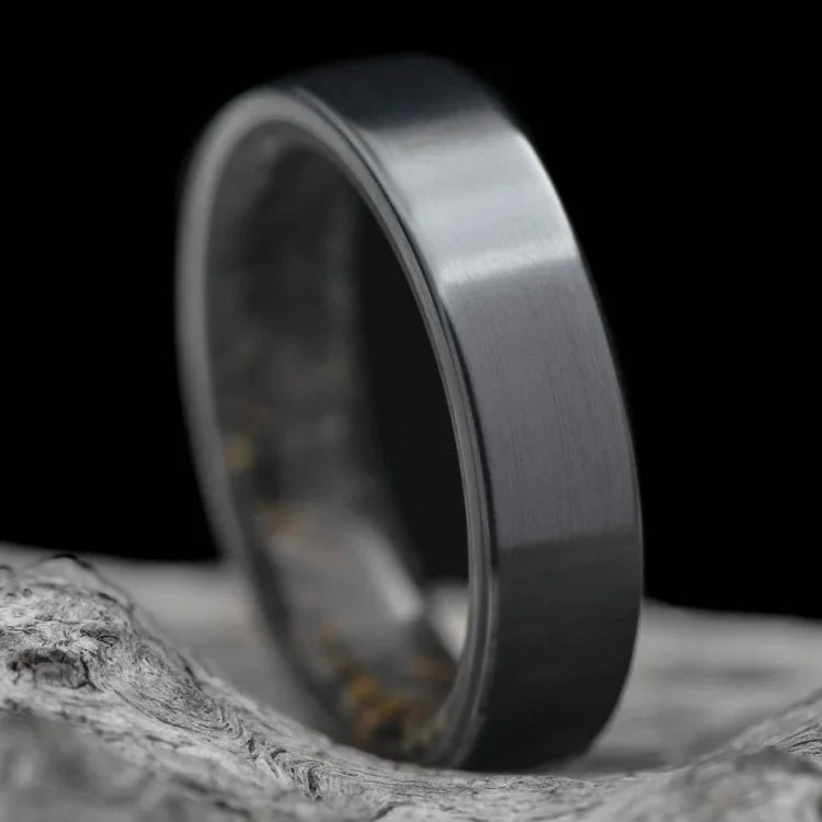 Black titanium wedding ring with dinosaur bone inner sleeve, 5mm width, custom engraving available, unique simple design, displayed on a white sea branch.