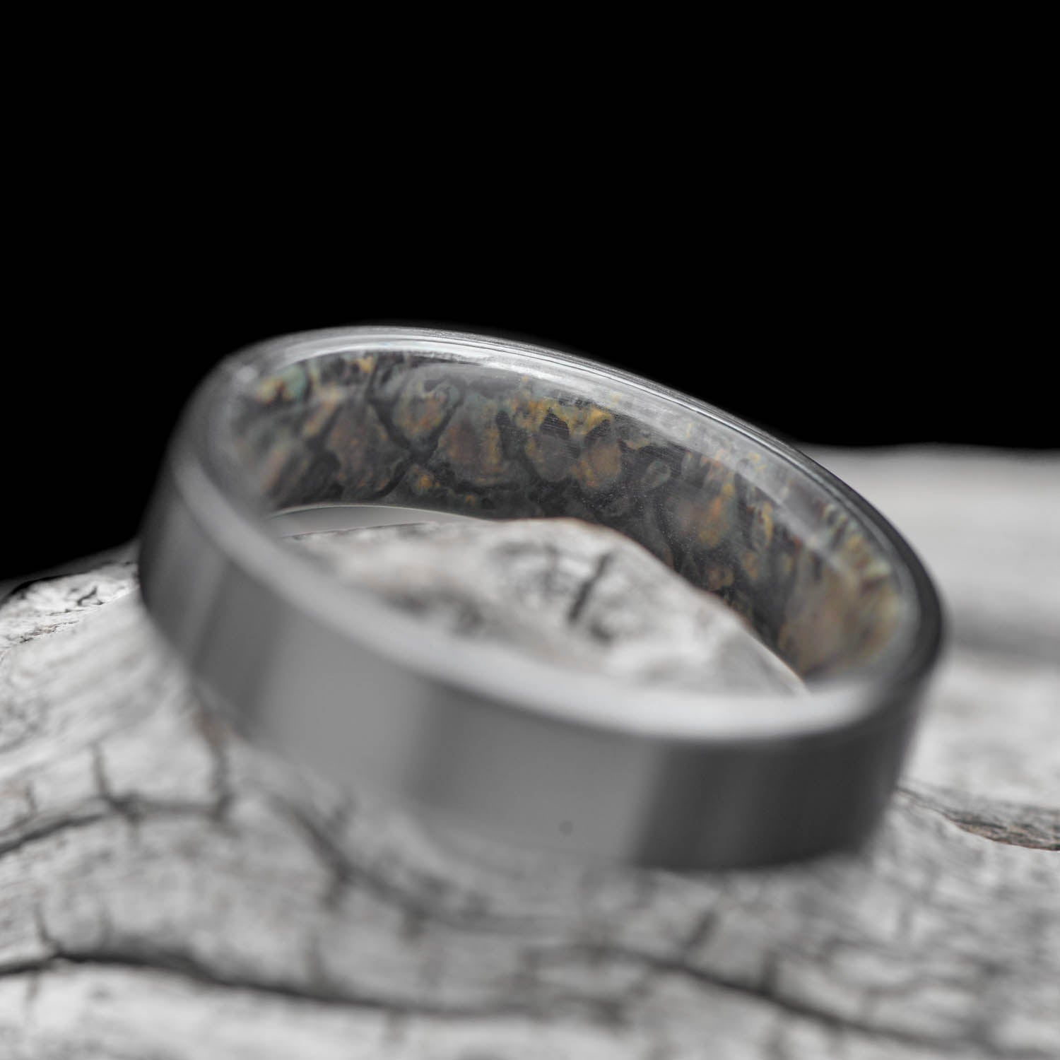 Black titanium wedding ring with dinosaur bone inner sleeve, 5mm, custom band, unique and simple design, free engraving, displayed on white sea branch.