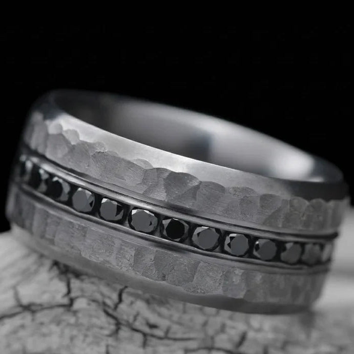Tantalum wedding band with eternity set precious stones, 10mm mens ring with faceted bevel profile, free engraving, displayed on a white sea branch.