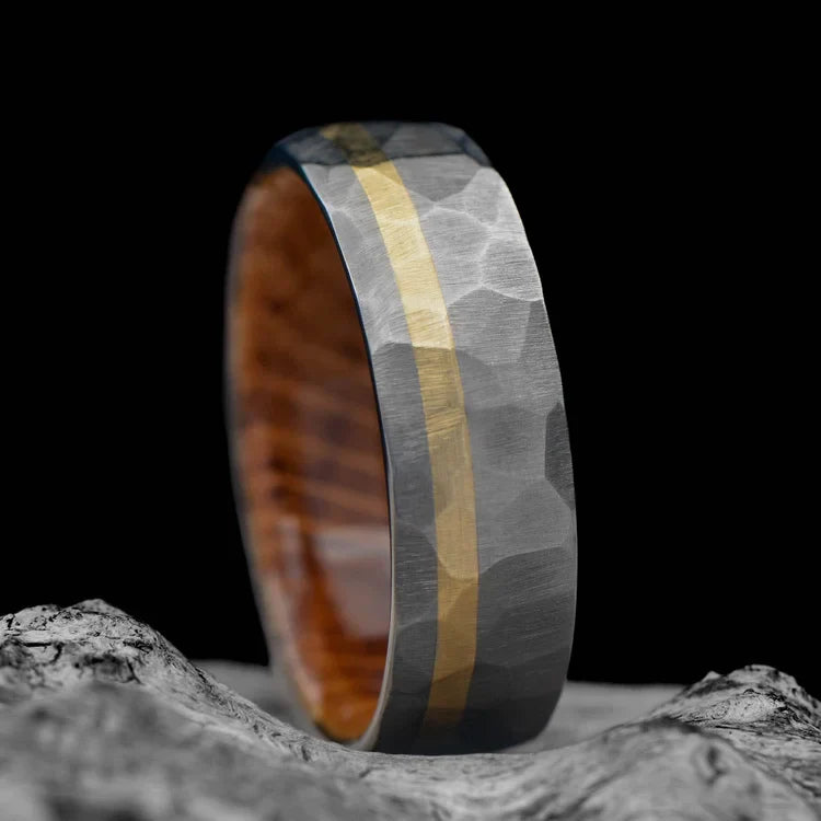 Titanium wedding band with 10K yellow gold and whiskey barrel oak inlay, unique faceted design, 7mm mens ring, displayed on a white sea branch, free engraving option available.