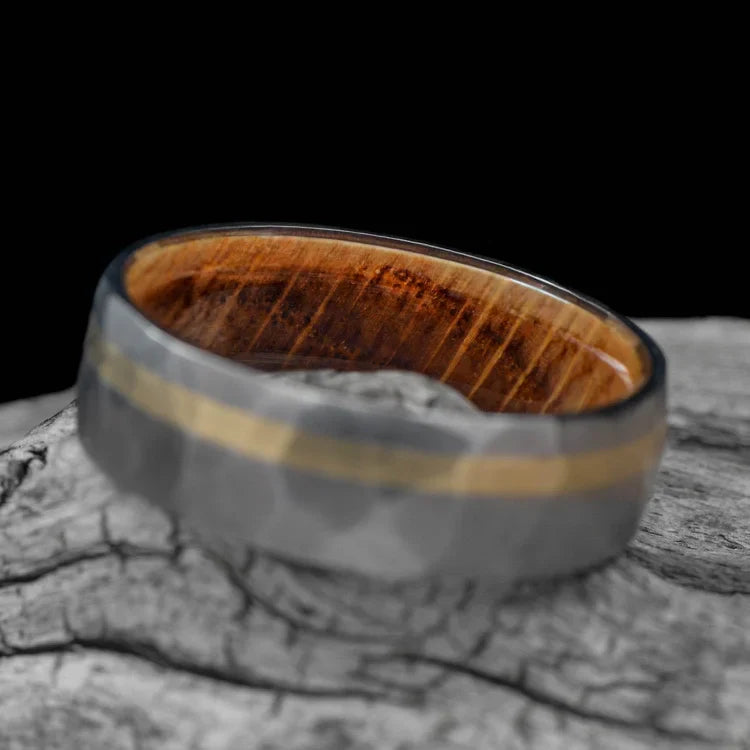 Titanium wedding band with 10KY gold and whiskey barrel oak inlay, featuring a unique faceted design, displayed on a white sea branch, 7mm mens ring with free engraving.