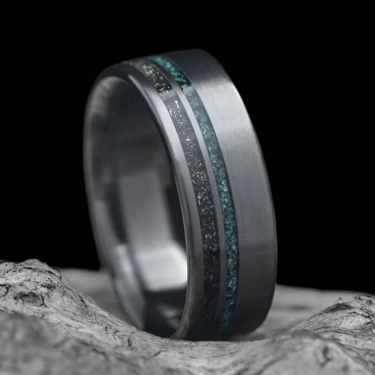 Black titanium wedding band with meteorite and moss agate inlays, featuring free engraving, 7mm width, mens unique ring, displayed on a white sea branch.