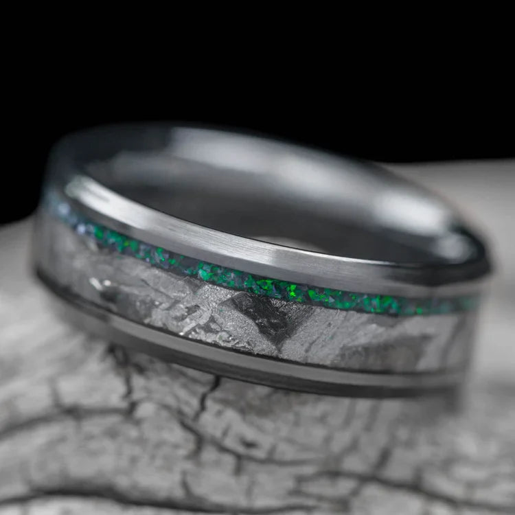 Black titanium wedding band with black emerald opal and meteorite inlays, 7mm mens ring, unique design, free engraving, displayed on a white sea branch.