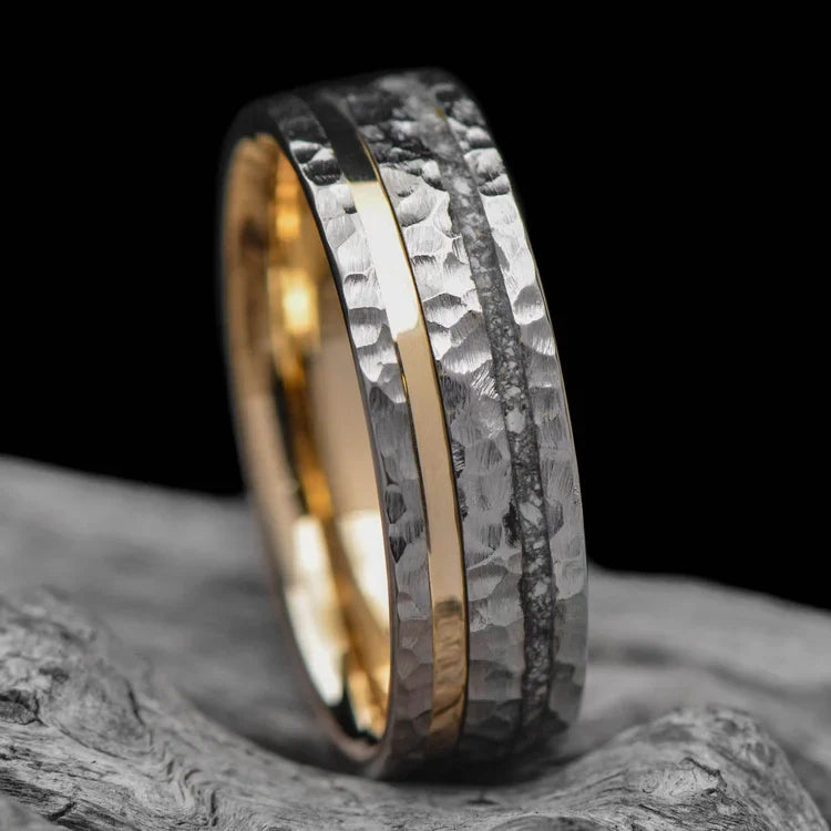 Titanium wedding band with 14K yellow gold and ashes inlays, free engraving, 7mm mens ring, faceted flat profile, unique design, displayed on a white sea branch.