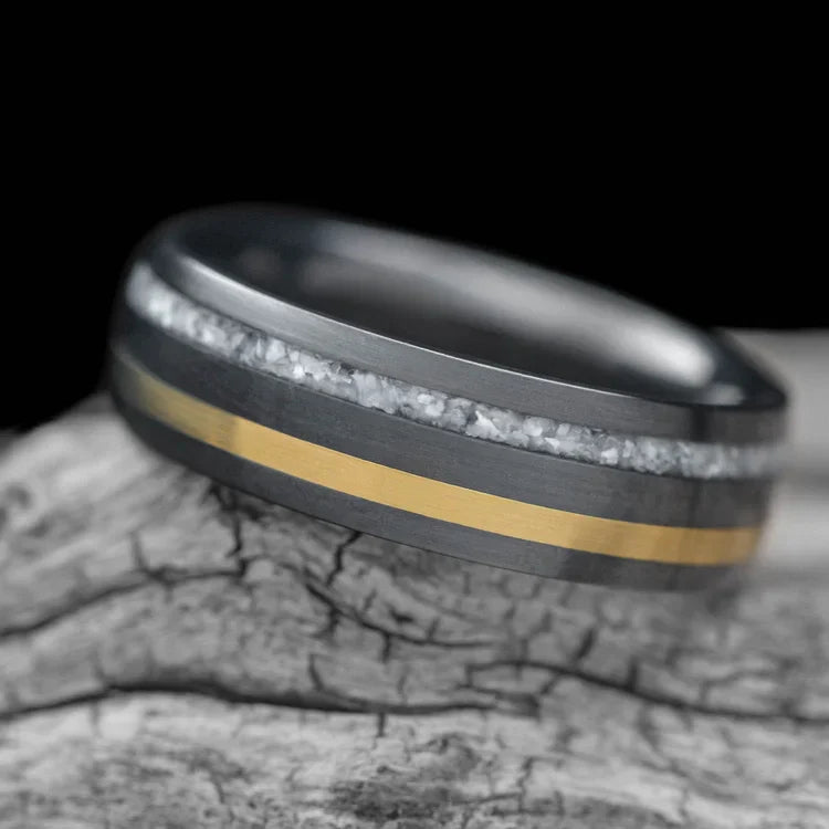 Black titanium wedding band with pearl and 18K yellow gold inlays, featuring free engraving, 7mm width, mens brushed domed profile, unique design, displayed on white sea branch.