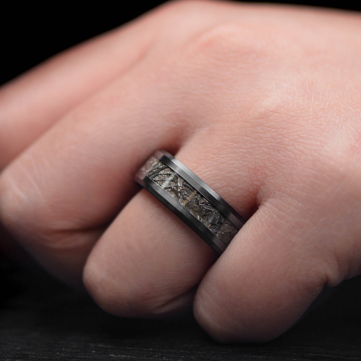 Black titanium mens wedding band with central meteorite inlay and bloodwood inner sleeve, 8mm width, displayed on a white sea branch, offering free engraving for a unique touch.