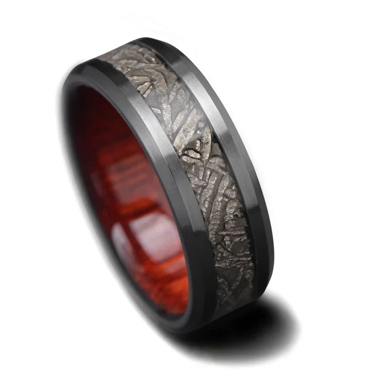 Black titanium ring featuring a central meteorite inlay and bloodwood inner sleeve, 8mm mens wedding band with free engraving, unique design on white background.