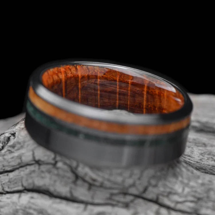 Black titanium wedding band with whiskey barrel oak and moss agate inlays, 8mm mens ring, unique custom design, free engraving, displayed on a white sea branch.