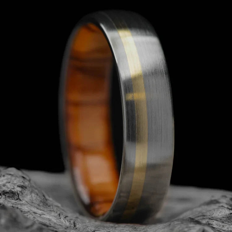 Titanium wedding band with 10K yellow gold and olivewood inlay, featuring a unique brushed domed profile, displayed on a white sea branch; mens 6mm ring with free engraving option.