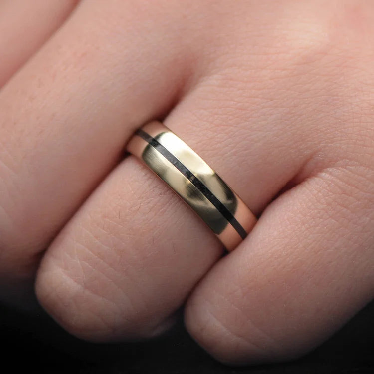 14K yellow gold mens wedding band with central black onyx inlay, 6mm brushed domed profile, unique design, free engraving, displayed on a white sea branch.