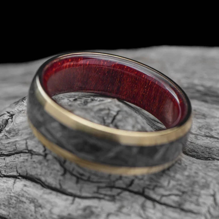 10KY gold wedding band with central meteorite inlay and bloodwood inner sleeve, 7mm mens ring, unique design, free engraving, displayed on white sea branch.