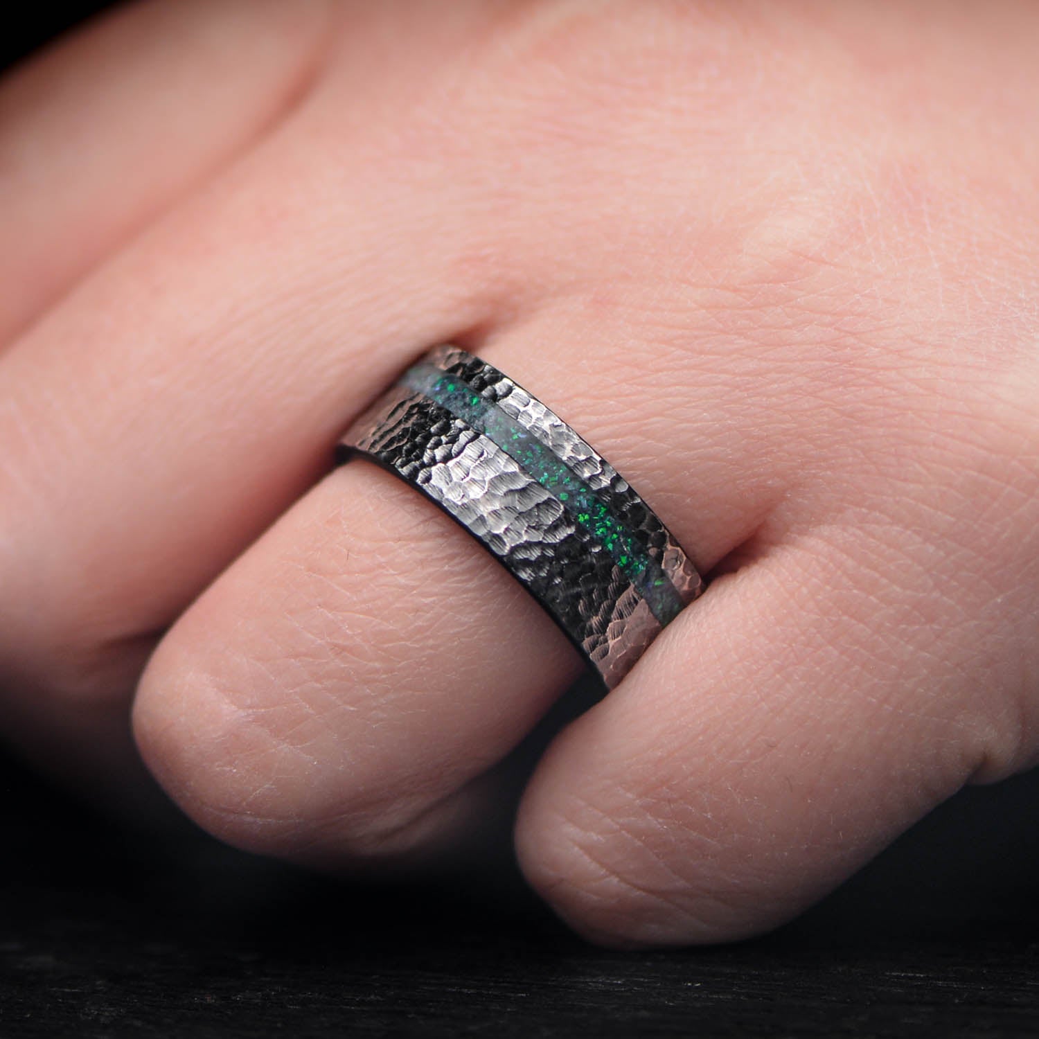 Black titanium wedding band with black emerald opal and malachite inlays, 9mm mens hammered flat profile ring, displayed on a white sea branch, free engraving available.