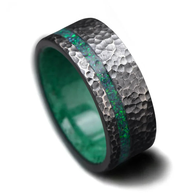 Black titanium mens wedding band with black emerald opal and malachite inlays, featuring a hammered flat profile, 9mm width, available with free engraving, displayed on a white background.