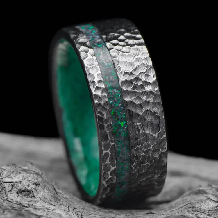 Black titanium wedding band with black emerald opal and malachite inlays, 9mm mens hammered flat profile ring, displayed on a white sea branch, free engraving available.