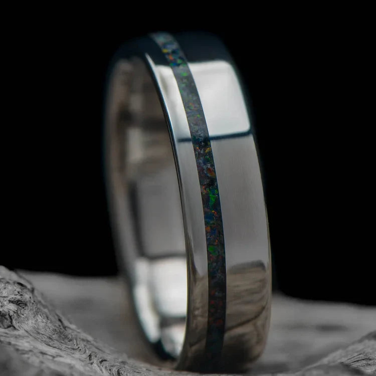 Titanium wedding band with black fire opal inlay, 5mm custom simple ring, polished flat profile, free engraving, displayed on a white sea branch.