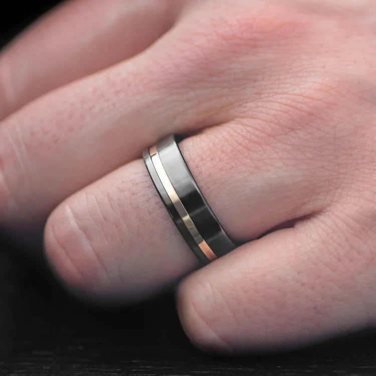 Mens 7mm black titanium wedding band with 18K yellow gold inlay and olivewood inner sleeve, brushed flat profile, free engraving option, on a white background.