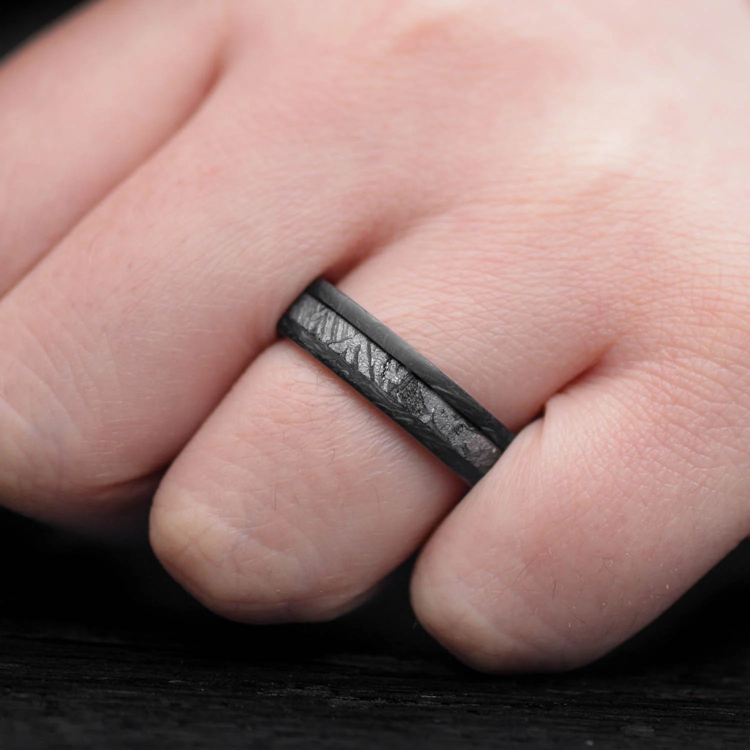 Mens wedding band featuring a forged ring design with a solid meteorite central inlay and whiskey barrel oak sleeve, shown on a hand; unique 6mm mens ring with free engraving option.