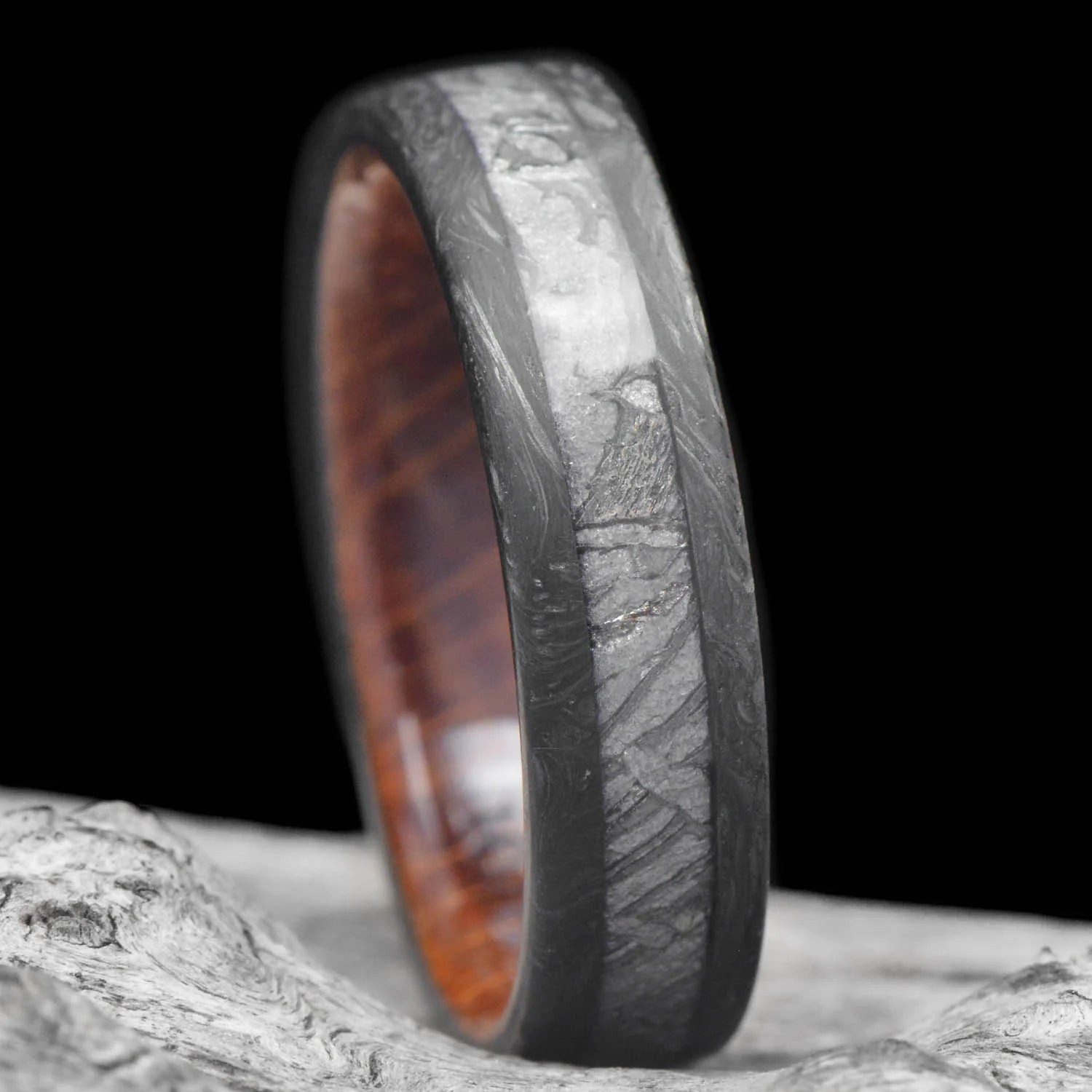 Mens wedding band featuring a solid meteorite central inlay and whiskey barrel oak sleeve, displayed on a white sea branch, 6mm unique forged ring with free engraving option.