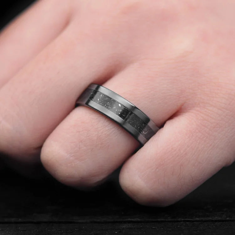 Hand wearing a Black Titanium Wedding Band with Meteorite and Sand Inlay, featuring a 7mm width and Black Fire Opal Inner Sleeve, perfect for mens wedding rings, available with free engraving.