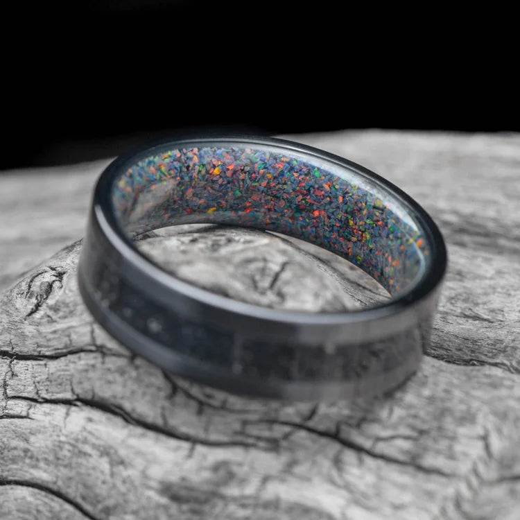 Black Titanium Wedding Band with Meteorite and Sand Inlay, featuring a Black Fire Opal Inner Sleeve, 7mm Mens Wedding Ring, displayed on a white sea branch.