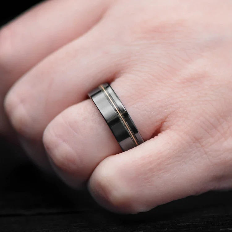 Mens black titanium wedding band with moss agate and guitar string inlays, featuring a deer antler inner sleeve, worn on a hand, 7mm width, free engraving available.