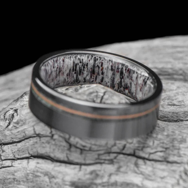 Black titanium wedding band featuring moss agate and guitar string inlays, 7mm mens ring with deer antler inner sleeve, displayed on a white sea branch, free engraving available.