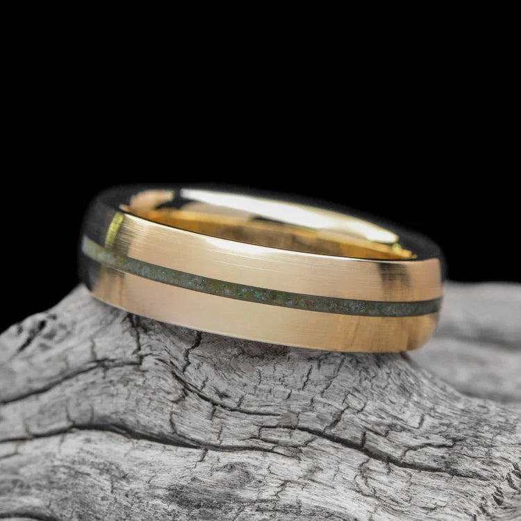 14K yellow gold mens wedding band with custom inlay and central emerald, brushed domed design, 6mm width, free engraving, displayed on a white sea branch.