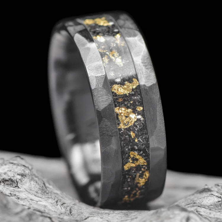 Black titanium mens wedding band with central meteorite and gold leaf inlay, 8mm, unique design, free engraving, displayed on white sea branch.