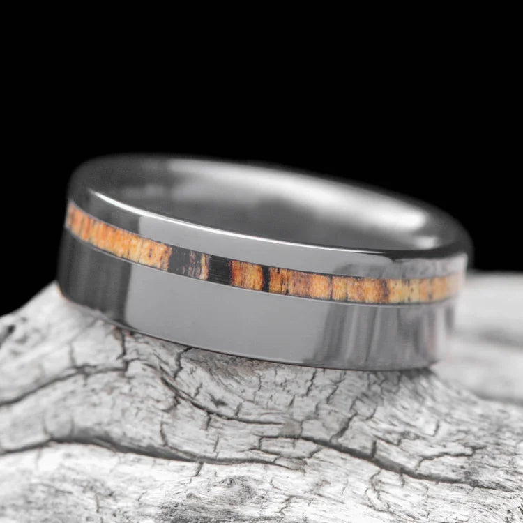 Black titanium wedding band with silver spalted birch inlay, 7mm mens custom ring, displayed on a white sea branch, free engraving available.