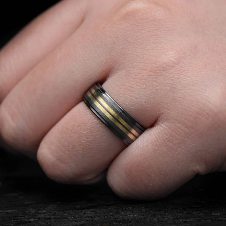 Mens black titanium wedding band with dual 18K yellow gold inlays, featuring a brushed step profile, shown on a hand; 7mm custom mens ring with free engraving option.