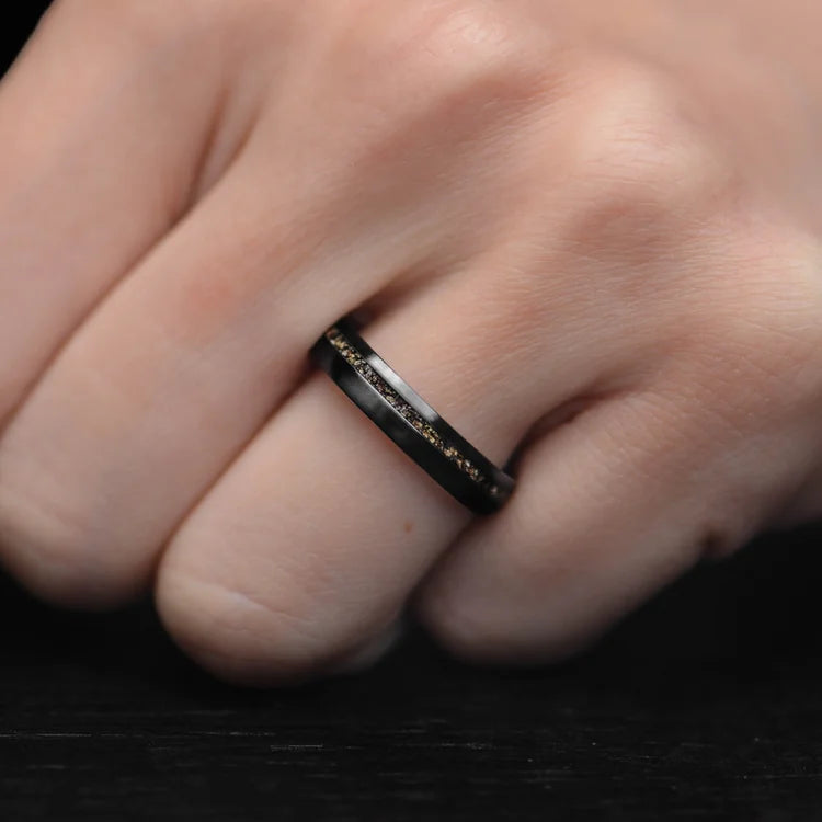 Black titanium wedding ring with crushed T-Rex inlay on a hand, featuring a brushed domed profile and custom engraving, 4mm unique simple band.