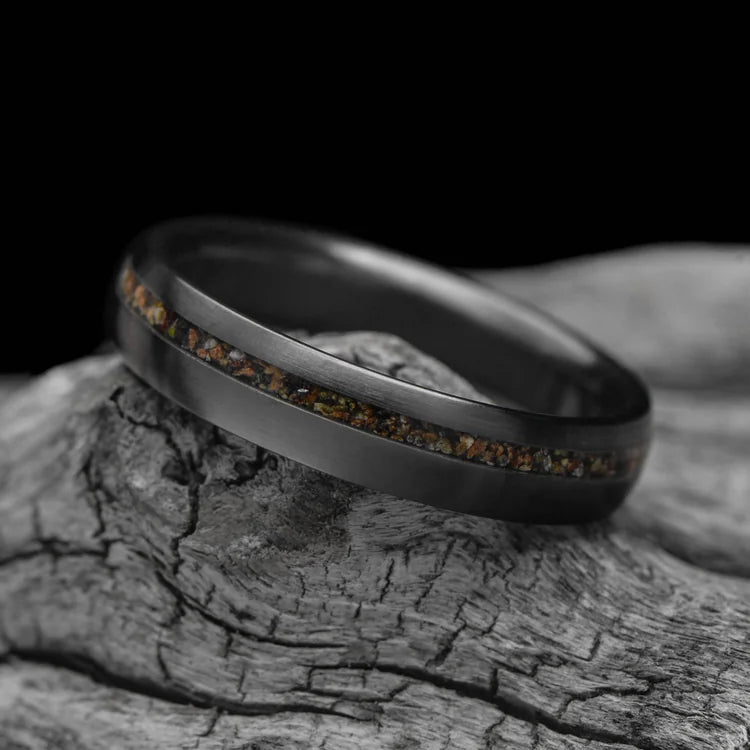 Black titanium wedding ring with crushed T-Rex inlay, 4mm brushed domed profile, unique simple design, custom engraving available, displayed on white sea branch.