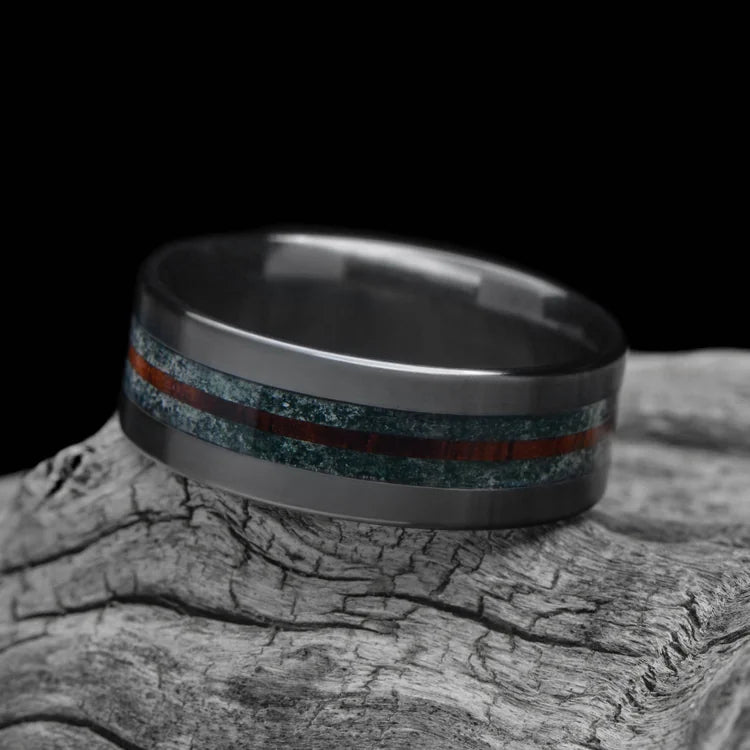 Black titanium wedding band with moss agate and central koa inlay, 8mm mens ring, unique design, free engraving, displayed on a white sea branch.