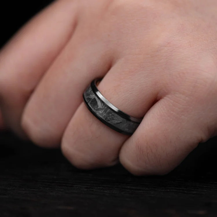 Mens 7mm black titanium wedding band with solid meteorite central inlay and oak inner sleeve, featuring brushed beveled edges, shown on a hand. Free engraving available.