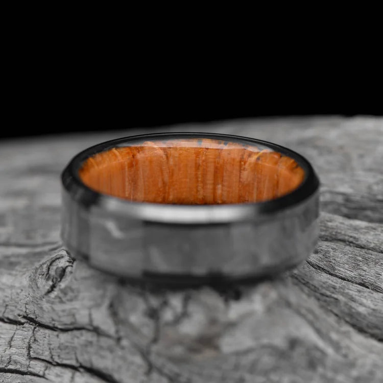 Black titanium wedding band with solid meteorite central inlay and oak inner sleeve, 7mm mens ring, brushed beveled edges, free engraving, displayed on a white sea branch.