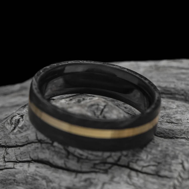 Forged wedding band with 10KY inlay and African blackwood inner sleeve, mens 7mm brushed flat profile ring, free engraving, displayed on white sea branch.