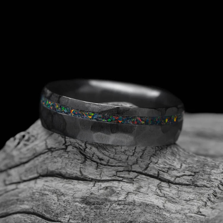 Black titanium ring with black fire opal inlay, 6mm mens wedding band, faceted domed profile, unique mens ring, displayed on a white sea branch.