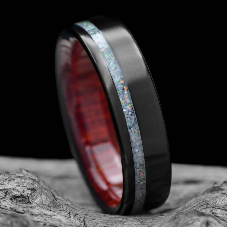 Black titanium mens wedding ring with pearl opal inlay and bloodwood inner sleeve, polished flat profile, 6mm width, displayed on white sea branch, free engraving available.