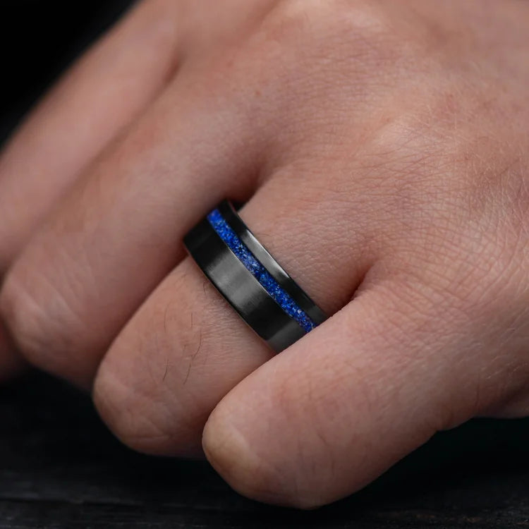 Hand wearing an 8mm black titanium mens wedding band with lapis lazuli inlay, featuring a brushed flat profile and unique design, available with free engraving.