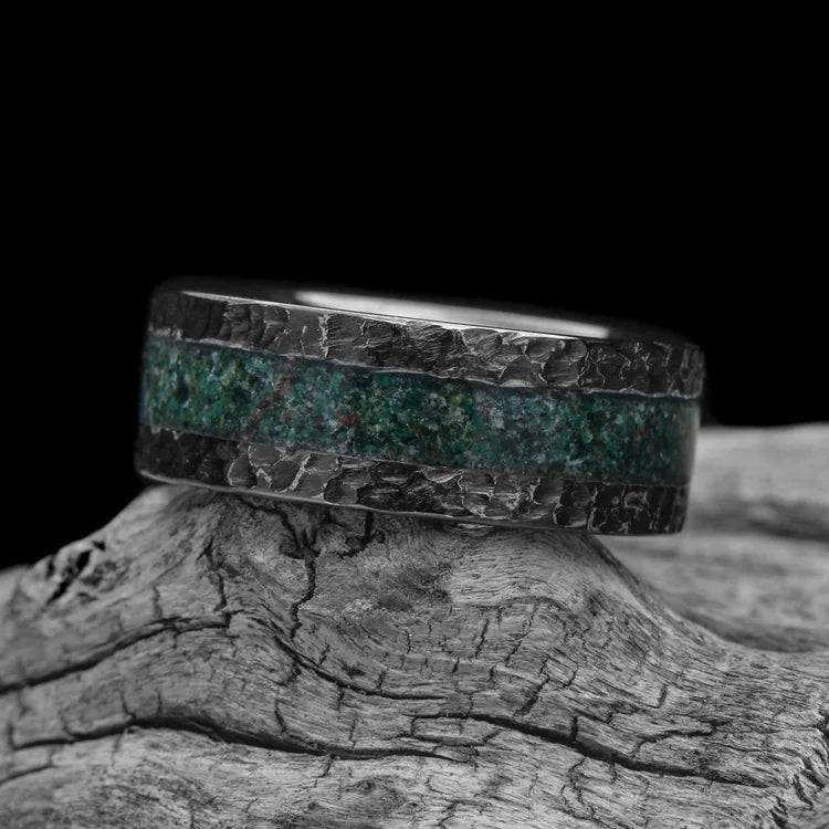Black titanium mens wedding band with central moss agate inlay, featuring a unique hammered flat profile, 8mm wide, displayed on a white sea branch.