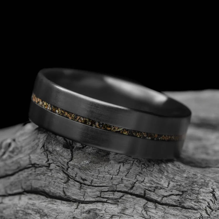 Zirconium ring with central crushed T-Rex inlay, 7mm mens wedding band, unique brushed flat profile, laying on white sea branch, free engraving available.