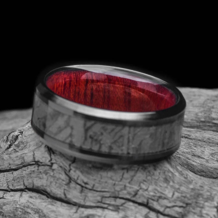 Black titanium ring featuring a central meteorite inlay and bloodwood inner sleeve, 8mm mens wedding band with free engraving, unique design on white background.