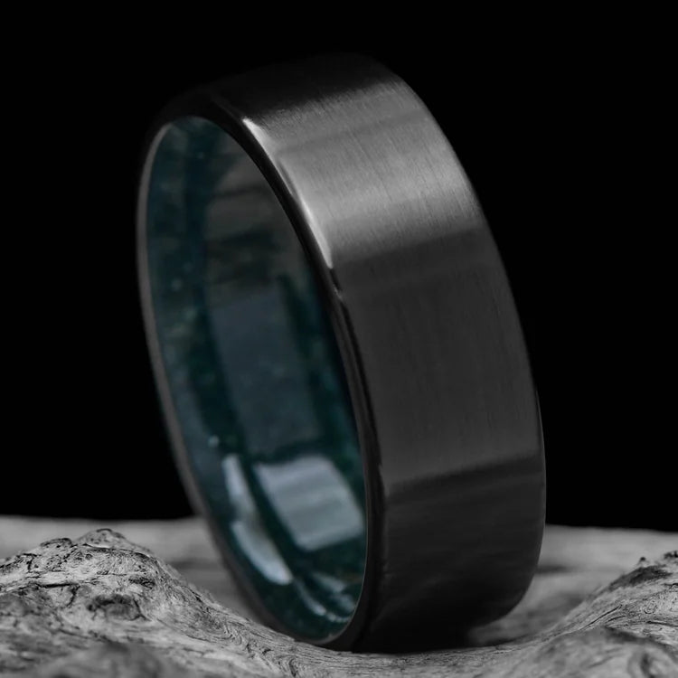 Black titanium wedding band with brushed finish and moss agate inner sleeve, 8mm mens ring, unique design, displayed on a white sea branch, free engraving available.