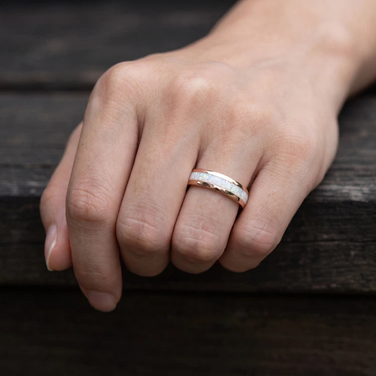 Hand wearing a polished 6mm domed mens wedding band with a central pearl opal inlay, crafted in 10K rose gold.