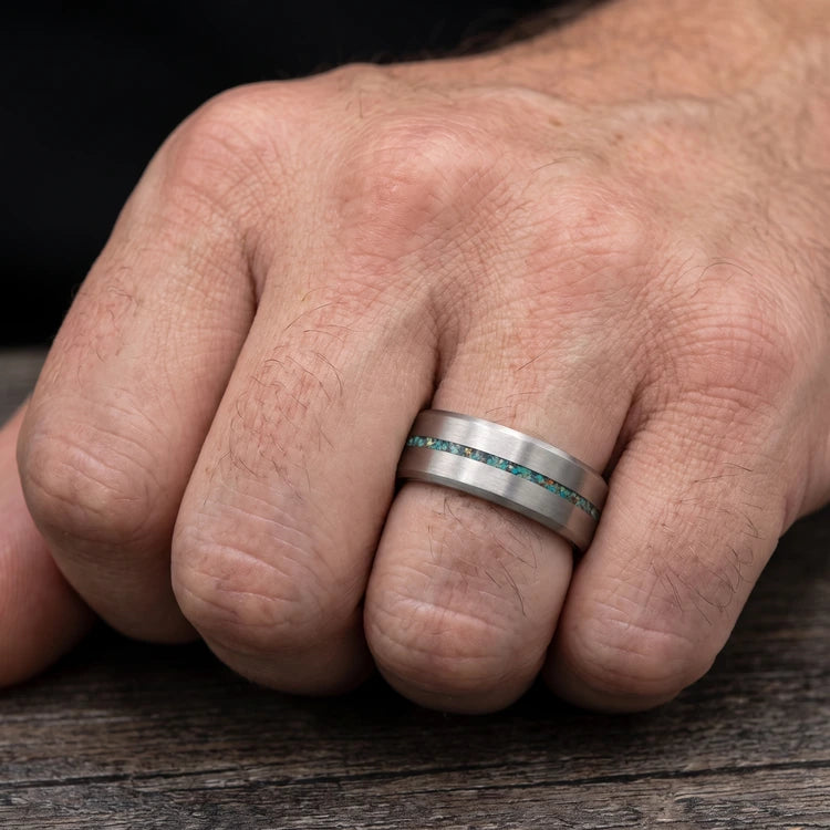 Hand wearing an 8mm mens tantalum wedding band with a central turquoise inlay, brushed finish and beveled edges.
